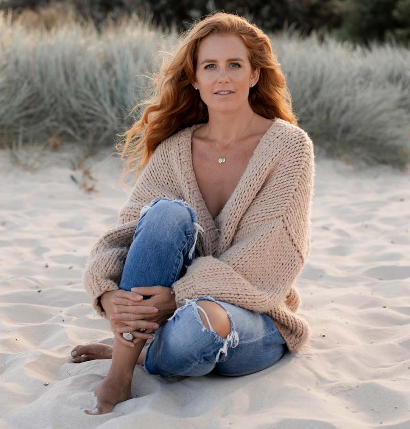 Caitlin Cady sitting on the beach at dusk and smiling softly at the camera